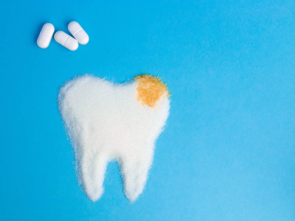 Tooth from white and bown sugar with pils on blue background, symbol - Fotografie, Obrázek