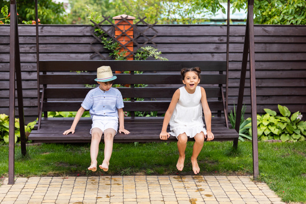 cute kids sitting on wooden bench together on backyard on summer day - Zdjęcie, obraz