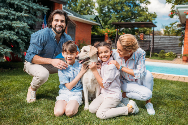 ευτυχισμένη οικογένεια με σκυλί λαμπραντόρ βλέπουν φωτογραφική μηχανή ξοδεύοντας το χρόνο στην πίσω αυλή του σπιτιού χώρας θερινή ημέρα - Φωτογραφία, εικόνα