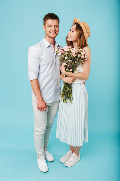 Image of young happy caucasian people man and woman isolated over blue background holding flowers. - Valokuva, kuva