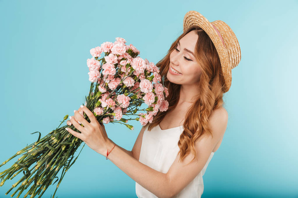 Image of young happy caucasian woman isolated over blue background holding flowers. - Foto, Bild