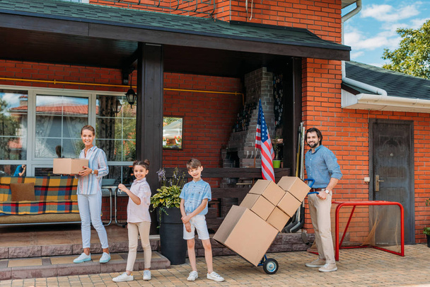 Eltern mit Pappkartons und Kindern stehen am Landhaus und ziehen nach Hause - Foto, Bild