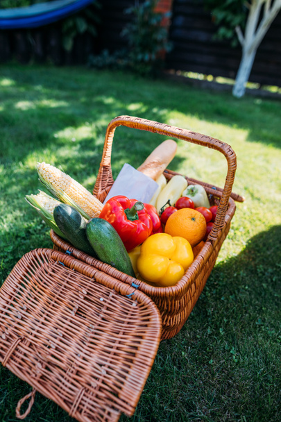 close up view of basket with baget and vegetables for picnic on green grass - Foto, Bild