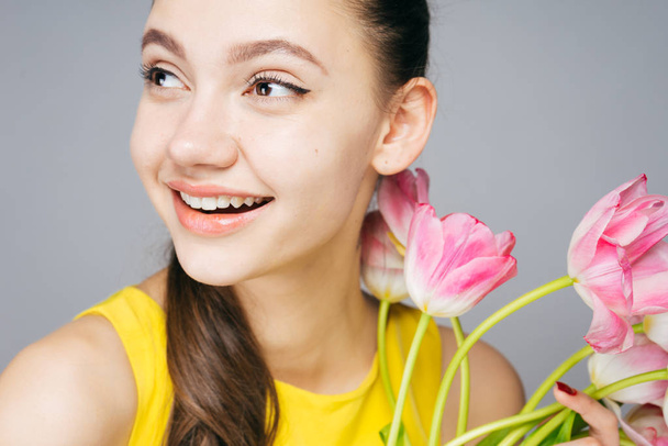 joyful charming girl with white teeth smiling, enjoying the spring, holding a bouquet of fragrant flowers - Photo, Image