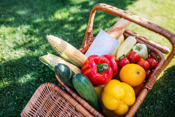 close up view of basket with baget and vegetables for picnic on green grass - Photo, Image