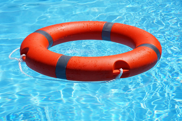 Red lifebuoy pool ring float on blue water. Life ring floating on top of sunny blue water. Life ring in swimming pool - Photo, Image