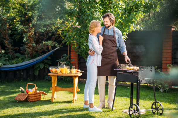 smiling couple having barbecue on backyard on summer day - Fotografie, Obrázek