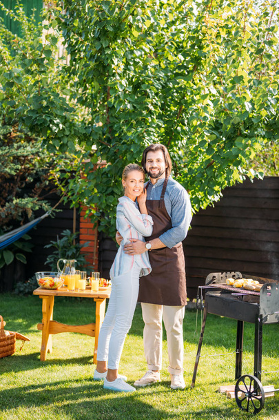 smiling couple looking at camera having barbecue on backyard on summer day - Фото, зображення