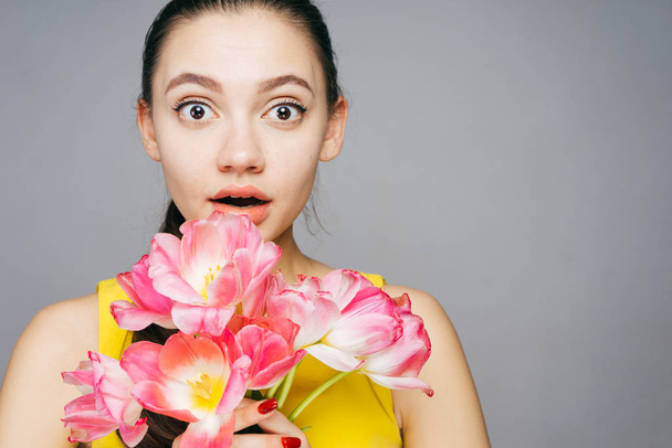 surprised beautiful young girl looking into the camera, holding fragrant pink flowers - Фото, зображення