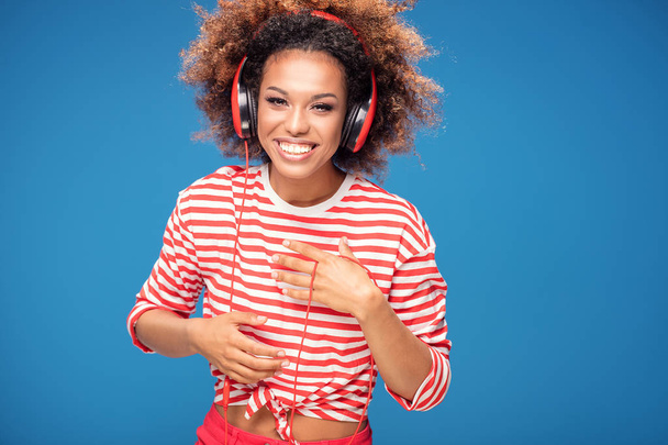 Adorable african american woman with red headphones laughing out loud, blue background. - Foto, imagen