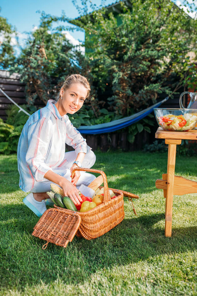 woman with basket full of fresh vegetables for picnic on backyard - Foto, afbeelding