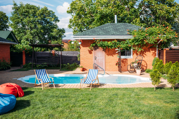 casa de campo com gramado verde, piscina e cadeiras de praia no quintal
 - Foto, Imagem