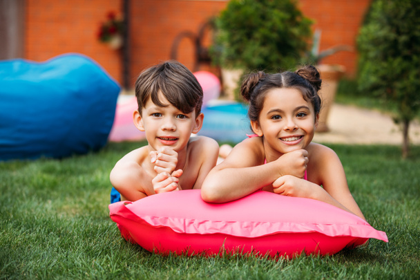 portrait of cute kids resting on inflatable mattress on green lawn on backyard of country house - Photo, Image