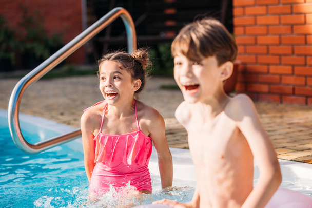 emotional little siblings swimming in swimming pool together on summer day - Fotó, kép