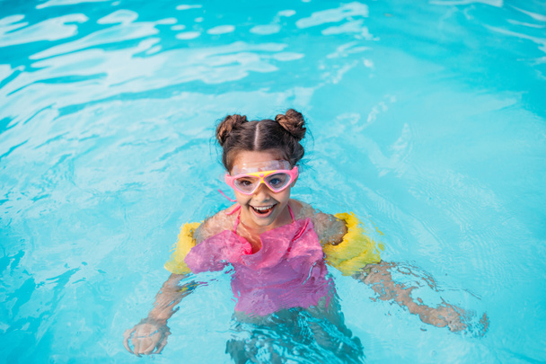 портрет улыбающегося ребенка в маске с водяным крылом, плавающим в бассейне в летний день
 - Фото, изображение