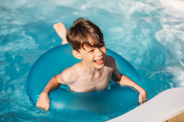 portrait of happy boy with inflatable ring swimming in swimming pool on summer day - Foto, Bild