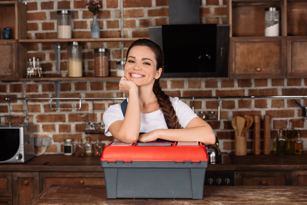 smiling young repairwoman leaning on toolbox and looking at camera - Photo, image