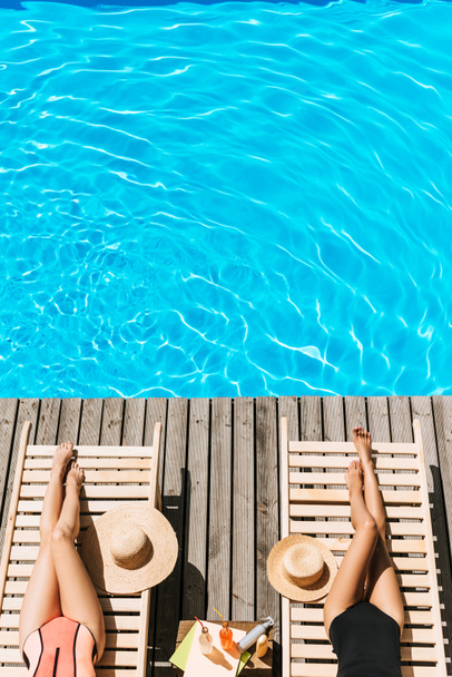 tiro recortado de mujeres jóvenes en traje de baño descansando en chaise lounges cerca de la piscina
 - Foto, Imagen