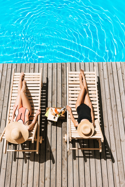 high angle view of young girlfriends lying on chaise lounges near swimming pool    - Photo, Image