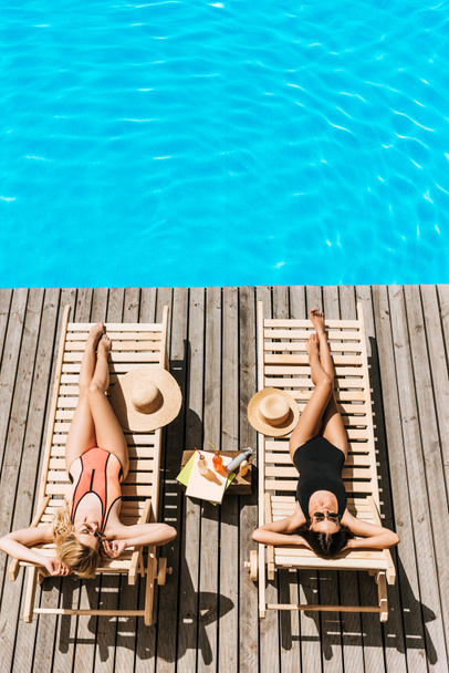 high angle view of young women tanning on chaise lounges near swimming pool   - Foto, Bild