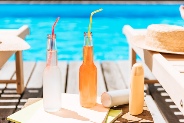 close-up view of bottles with summer drinks, sunscreen and chaise lounges at swimming pool - Foto, Imagem