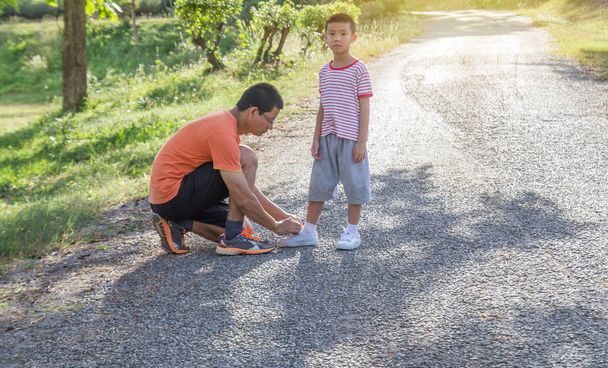 Papa schnürt seinem Sohn auf der Straße im Park die Seilschuhe. at mit Sonnenlicht Hintergrund.  - Foto, Bild