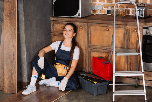 lächelnde junge Reparaturfachfrau entspannt auf dem Fußboden in der Küche - Foto, Bild