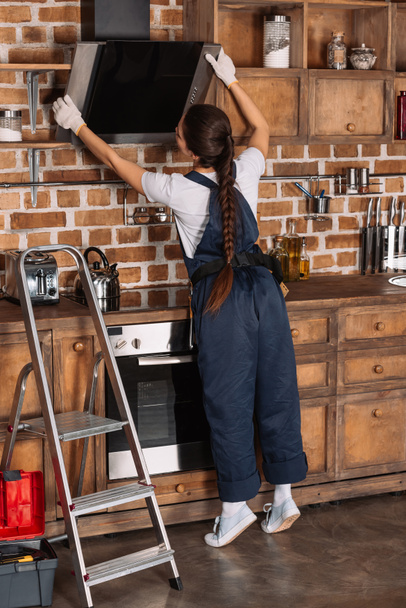 young repairwoman in overall examining stove hood at kitchen - Photo, Image