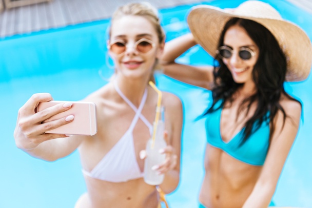 beautiful young girlfriends taking selfie with smartphone at poolside  - Фото, зображення