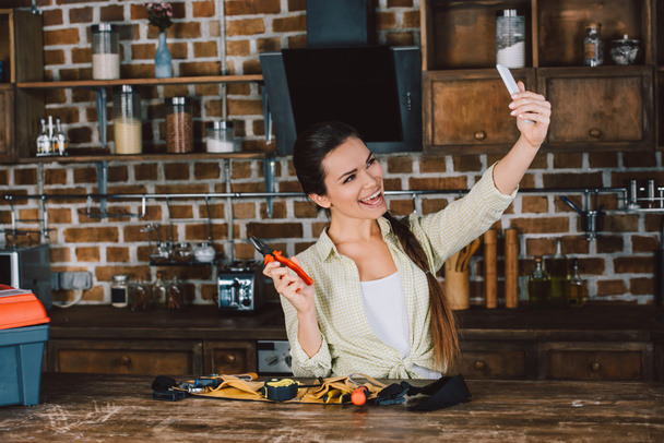 feliz jovem mulher tomando selfie com alicate na cozinha
 - Foto, Imagem