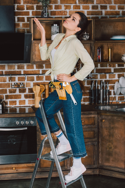 beautiful young repairwoman standing on stepladder at kitchen and looking up - Фото, зображення