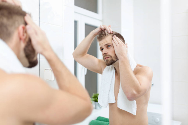 Handsome unshaven man looking into the mirror in bathroom - Фото, зображення