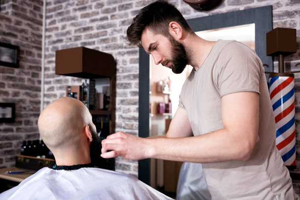 Professional Master hairdresser cuts client beard in barbershop - Foto, Bild