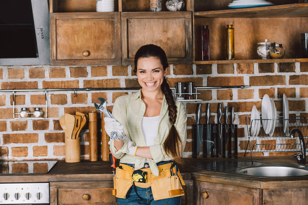 Glückliche junge Reparaturfrau mit Schraubenschlüssel steht in der Küche - Foto, Bild