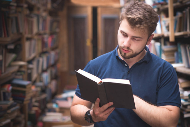 Чоловічий портрет тримає книгу в його руках і він читає на тлі стара, атмосферних, публічна бібліотека. Студентів читає книгу в старому затишна бібліотека. Пошук і вибір книг в бібліотеці - Фото, зображення