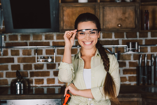 Glückliche junge Reparaturfrau mit Schutzbrille blickt in die Kamera - Foto, Bild