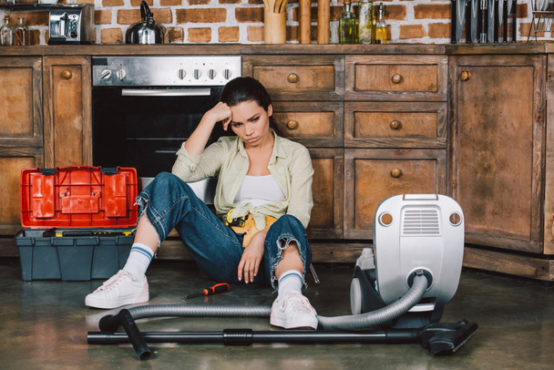 mladá žena sedící na podlaze kuchyně s vysavačem v depresi - Fotografie, Obrázek