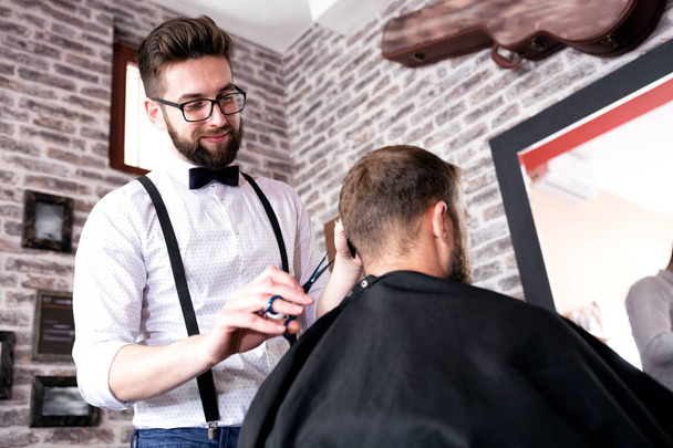 Hairdresser cutting a client's hair with scissors in a male barber shop - Zdjęcie, obraz