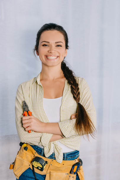 happy young repairwoman with pliers looking at camera - Foto, imagen
