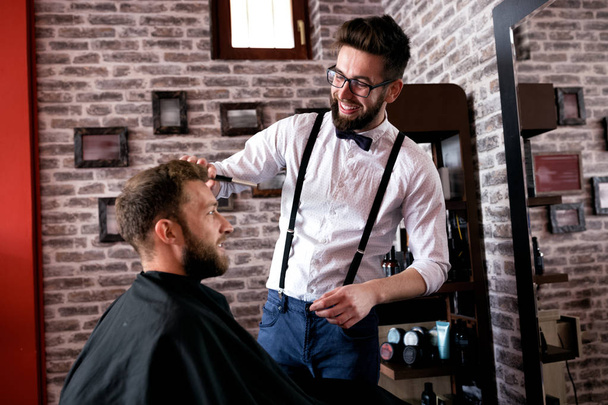Hairdresser adjusts hair a customer with a comb in barbershop salon - 写真・画像