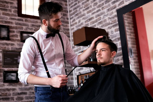 Hairdresser adjusts hair a customer with a comb in barbershop salon - Fotografie, Obrázek