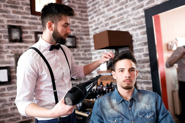 Hairdresser adjusts hair a customer with a comb and hairdryer  - Zdjęcie, obraz