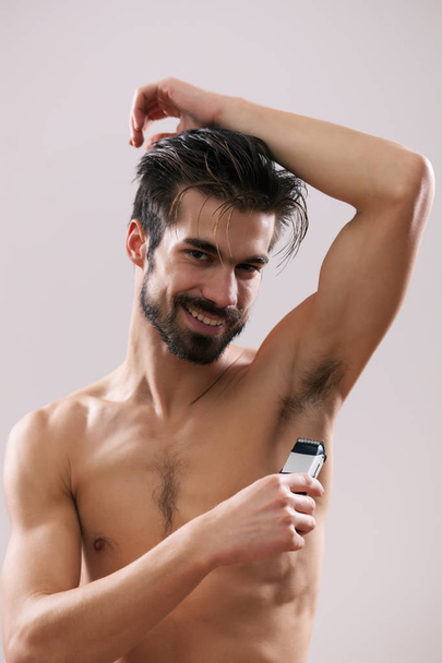 Joven hombre guapo se afeita la axila con afeitadora eléctrica
.  - Foto, imagen