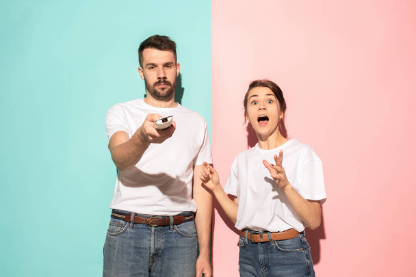Closeup portrait of young couple, man, woman. One being excited happy smiling, other serious, concerned, unhappy on pink and blue background. Emotion contrasts - Foto, Imagem
