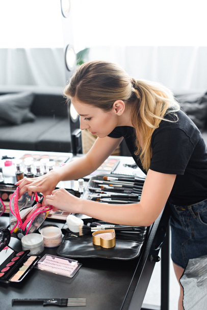 Seitenansicht des Maskenbildners auf der Suche nach Kosmetik in Kosmetikerin während der Arbeit - Foto, Bild