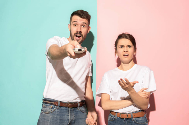 Closeup portrait of young couple, man, woman. One being excited happy smiling, other serious, concerned, unhappy on pink and blue background. Emotion contrasts - Φωτογραφία, εικόνα