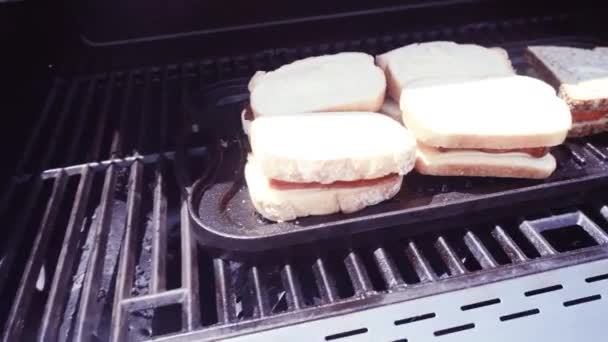 Grilling grilled cheese sandwich with bacon strips and fresh tomato on outdoor gas grill - Footage, Video