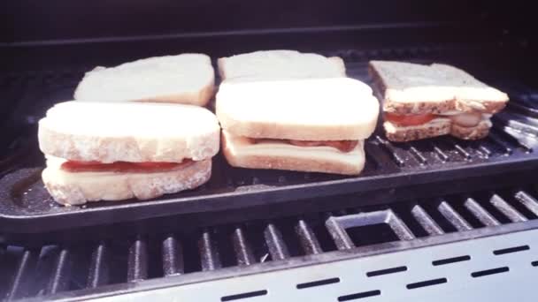 Panino al formaggio grigliato con strisce di pancetta e pomodoro fresco sulla griglia a gas all'aperto
 - Filmati, video