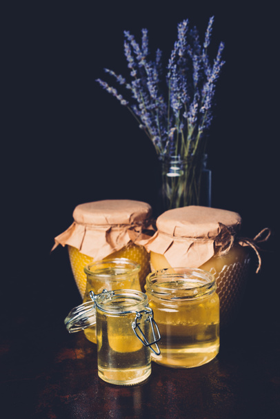 selective focus of lavender and various jars with honey on black background - Valokuva, kuva