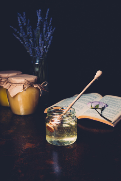selective focus of jar with honey stick and lavender on black background  - 写真・画像